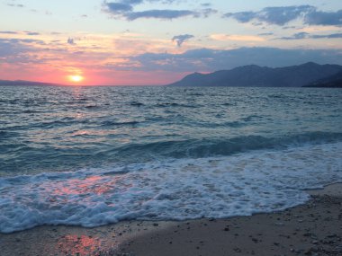 Bir yaz akşamında deniz manzaralı sahil, Hırvatistan, Dalmaçya, Brela. Deniz kenarında akşam, ufuktaki pembe güneş kumsaldaki deniz köpüğüne yansıyor.,