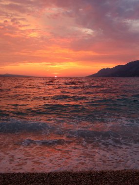 Sahilde gün batımı, kırmızı-turuncu deniz ve bulutlu gökyüzü, Brela, Hırvatistan, Dalmaçya. Gün batımında deniz manzarası, yaz akşamında gün batımında bulutlar, plaj tatili.