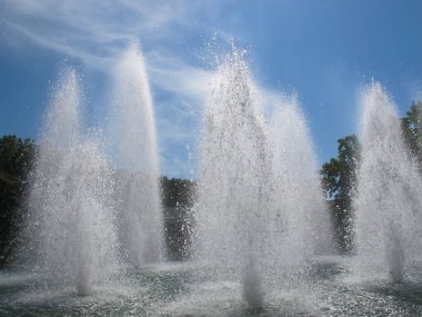 Mavi gökyüzüne karşı güçlü su fışkırtan çeşme. Şehir parkında bir yaz günü güneş ışınlarında güzel bir çeşme sıçraması.