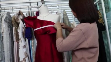 Asyalı bir terzi, bir terzi, bir giyim tasarımcısı, doğru boyutu ayarlamak için müşterinin kırmızı gece elbisesine karşı mezura kullanır. Hizmet işi küçük işletme zevki.