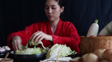 Kırmızı Hanbok yapan Asyalı bir kadının portresi. Titizlikle hazırlanmış bir kasede sebze ve tuz yoğuruyor. Taze ve temiz malzemelere dikkat ederek..