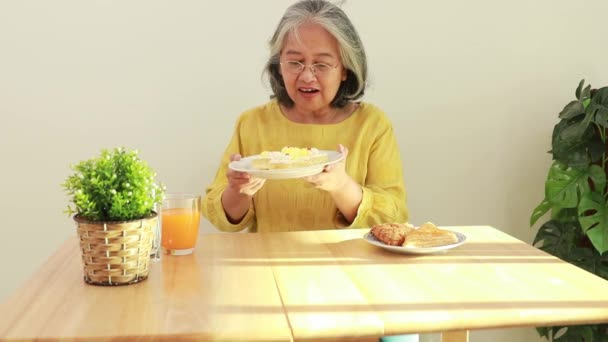 나이가 아시아 여자는 집에서 식사를 식탁에 있으며 스마트폰을 사용하여 전화번호부에 — 비디오