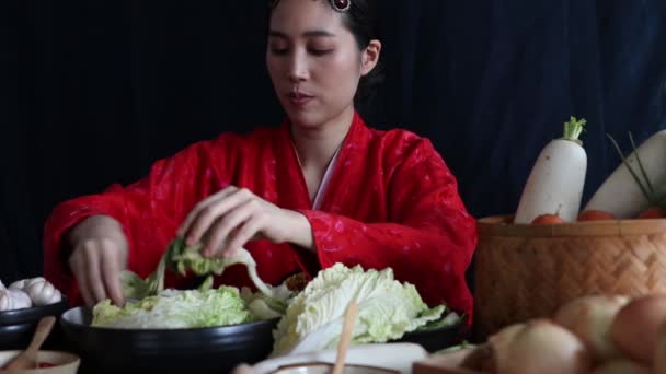 キムチを作る赤韓服を着たアジアの女性の肖像画 野菜や塩を手で練り 細心の注意を払って準備されたボウルに入れます 新鮮で清潔な食材に注意を払うことで — ストック動画