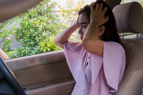 Asian woman parked her car because of stress, had a headache in the car with a debilitating problem, and she looked outside and reviewed something.