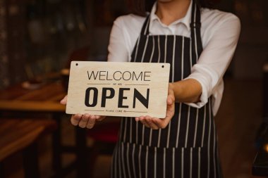 Kadın resepsiyonist, yiyecek ve içecek restoranında müşteri hizmetleriyle birlikte bir dükkan açılışı tabelası tutuyor.