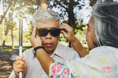Kör aşıklar kavramını önemseyen kıdemli çift: Kadın, kör ihtiyarın yanında ışığın ve ultraviyole ışınların kocasını sevgiyle yok etmesini engellemek için siyah gözlük takıyor..