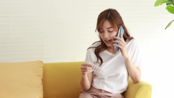 女性は薬剤師に助言を求めるために彼女のスマートフォンを使用する前に確認するためにビニール袋の丸薬を見て — ストック動画