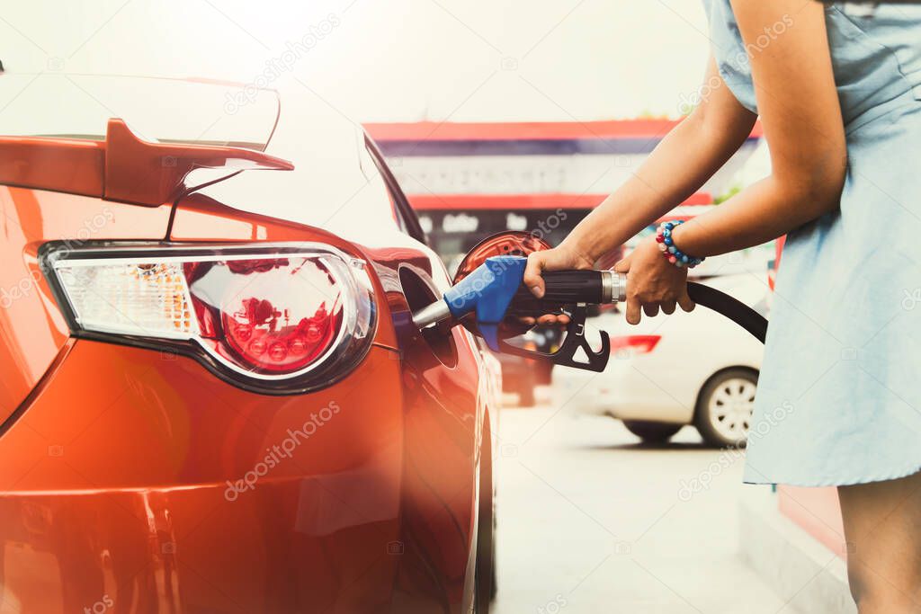Hands of a traveling woman driving her beautiful sports car to a gas station, holding injectors, fueling the car with standard quality clean gasoline at a self-service gas station.