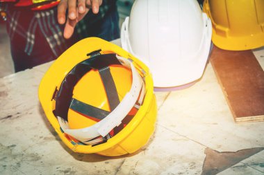 İşçiler sarı bir miğfer almak için ellerini kullanıyorlar. Kullanmak için ahşap masanın üzerinde baş aşağı.