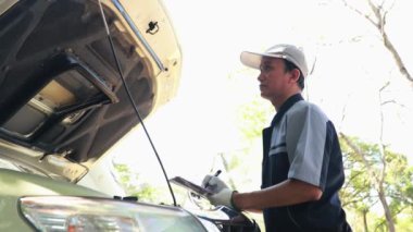 Profesyonel tamirciler, müşterilerin kamyonetlerini garajda inceler, bakım kayıtlarını yazmak için pano kullanır, motor durumunu ve yenilerinin gelmesi gereken ekipmanları kontrol eder.