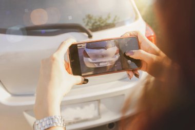 Genç bir kadın, trafik kazası sırasında arabanın plakasını kaydetmek için akıllı telefonu sigorta tazminatı olarak kullanıyor: kaza ve araba sigortası kavramı..