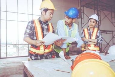 Fotoğraf bulanıklığı, saha mühendisi ekibi: Danışmanlık, iki erkek işçinin ve bir kadın mühendisin dinleyip kontrol altında tutulacağı bir inşaatın planlanması hakkında görüş alışverişinde bulunun. 