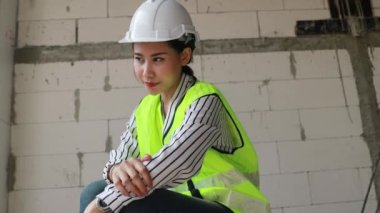 Güzel Asyalı kadın ustabaşı mimar inşaat alanında dizlerinin üstüne çöküp sessizce bir şey düşünüyor..