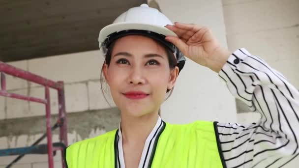 笑顔でカメラを見て肖像画の美しい女性建築家 白い安全ヘルメットを着て建設現場の建物で働くアジアの女性建築家のエンジニア — ストック動画