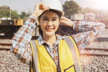 Tren bakım garajında çalışan Taylandlı kadın teknisyen: Güvenlik kaskına dokunan sevimli kadın mühendis kameraya bakıyor ve saha bakımına hazırlanırken gülümsüyor.