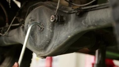 Bir araba servis merkezindeki erkek teknisyen kamyonun yeni arka diferansiyel vites yağının durumunu kontrol eder ve güvenlik ve düzeni sağlamak için kapak cıvatalarını yerleştirir..