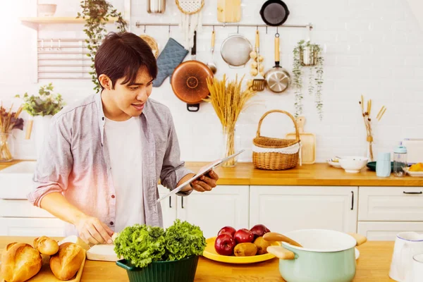 Solo show showcases handsome asian man using his laptop to practice cooking his own kitchen tricks by taking online lessons from the popular cooking show  : Soft focus