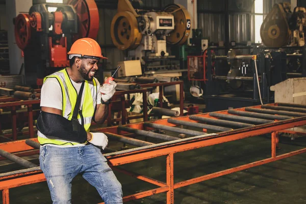 Male african american worker injured factory accident wears cast to work using walkie talkie reported injuries and arm pain unable to work to supervisors asking for help.