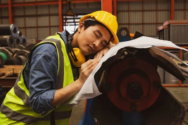 Asian male worker snoozing on blueprints at risk of accident and danger machinery work area : Male worker sleeps tired because of little rest and too much work.