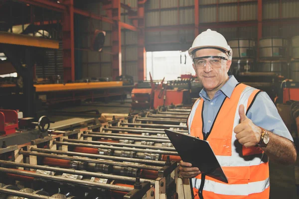 Senior chief engineer wearing goggles and helmet holding clipboard inspecting machinery and safety systems metal sheet factory standing in safe working area showing great thumbs up.