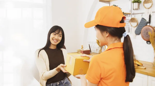 Female worker delivering parcels customer : Customer young woman standing at home picking up the parcel neatly holds the package and smiles happily : Success delivered to customers ordering online.