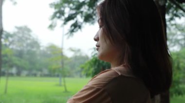 Parktaki çadırda yağmuru bekleyen Asyalı bir kadının portresi. İyi bir ruh hali içinde kameraya bakıyor. Gülümsüyor ve yağmur damlalarıyla oynuyor..