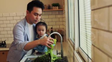 Asyalı şef babası, kızına bakıyor. Ev işi yapıyor. Zehirli yeşil sebzeleri mutfakta yıkıyor..