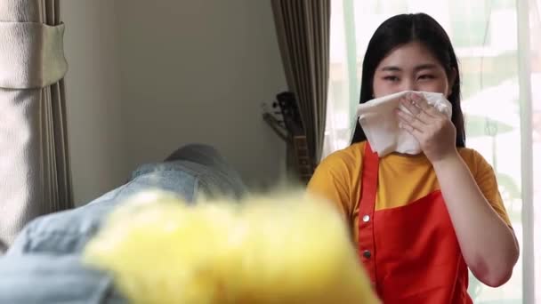 年轻的亚洲女人不戴面具做家务活 她们用粉碎机把沙发和窗户上的灰尘弄得满满的都是灰尘 用纸巾捂住鼻子以防灰尘 — 图库视频影像