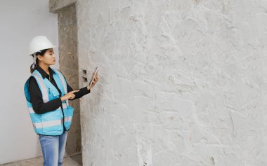 İnşaat alanında beton duvarlar tasarlayan Asyalı kadın mimarlar dizüstü bilgisayar kullanıyor ve seramik ya da ham beton kullanmak istiyor. Müşteriler için karar verme aşamasında..