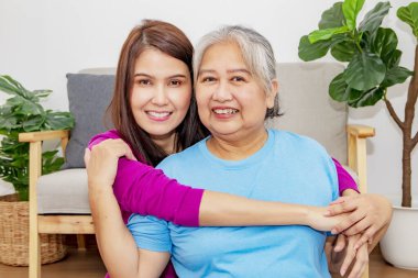 Minnettar kız güzel, yaşlı anneye oturma odasında sevgiyle sarılıyor bin yıllık annenin sağlığıyla ilgileniyor. Mutlu olun. Kameraya bakıp gülümseyin..