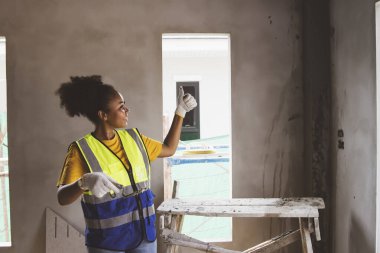 Yandan bakıldığında, son derece yetenekli Afrikalı Amerikalı kadın işçi inşaat alanındaki bir konutun duvarlarını sıvamış başarıya gururla bakıyor..