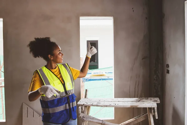 Side view Highly skilled African American female worker plastered the walls of a housing estate at the construction site looking at the work with pride thumbs up for success.
