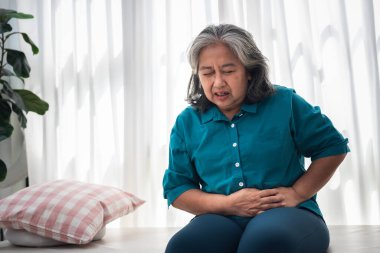 Yatakta oturan Asyalı bir kadın mide ağrısı çekiyor. Gastritis hastalığından dolayı, beyaz arka planda, geçici sağlık hizmetleri kavramından dolayı..