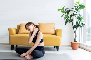 Asyalı çekici genç kadın, şu anda spor ve sağlık konseptine karşı beyaz geçmişiyle evdeki egzersizi sırasında boynundan sakatlanıyor..