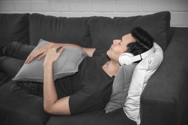 Asyalı, yakışıklı ve genç kulaklık takan, koltukta uzanan ve mutlu bir şekilde dinlenen, müzik konseptini dinleyerek rahatlayan insanlar. Bu resim kulaklıklara odaklanmış.