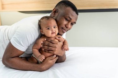 Afrikalı bir baba, Afrika ailesine ve yeni doğan siyah tenli bebeklere gülümseyen ve mutlu bir şekilde üç aylık bebeğini kucaklıyor ve koruyor..