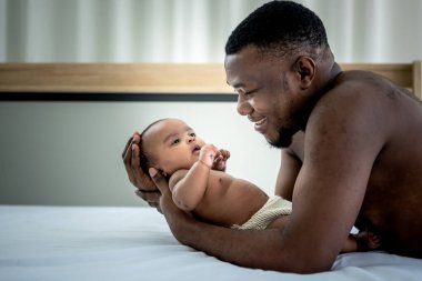 Afro-Amerikalı bir baba, kızının başını desteklemek için iki elini kullanırdı. Üç atlı yeni doğan oğlu, mutlu ve korunaklı bir yatak odasında uzanıyordu. Afrikalı aile ve yeni doğan bebek kavramı.