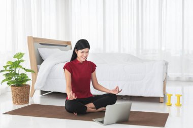 Çekici ve genç Asyalı kadın, çevrimiçi sınıflarda, beyaz yatak odasında, yeni normal ve çevrimiçi eğitim kavramında yoga yapıyor.