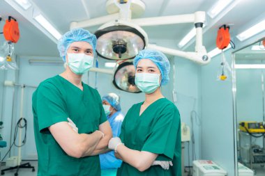 Asyalı doktor, erkek ve kadın cerrahlardan oluşan bir ekibin portre görüntüleri ameliyathanede duruyor, kadın hasta bulanık bir şekilde ameliyat yatağında oturuyor, sağlık hizmetleri ve ameliyat konseptine.