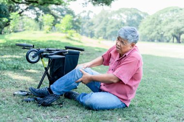 Yeşil çimlerde oturan Asyalı yaşlı adamın dizinin her iki tarafında da osteoporoz, emeklilik yaşı ve sağlık konsepti nedeniyle ağrılar var..
