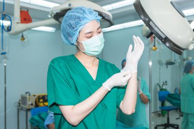 Asyalı kadın doktor ameliyathanede çalışıyor, ameliyat için tıbbi eldiven giyiyor, insanların sağlık ve estetik cerrahi konseptini inceliyor..