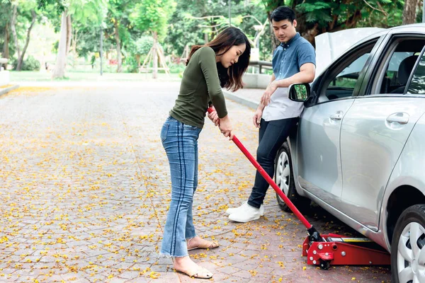 Asyalı çekici bir kadın, arabayı kaldırarak güzel parkta tek başına lastiği değiştiriyor, kocasını bulanık bir şekilde, güçlü bir kadına ve ulaşım konseptine dönüştürüyor..
