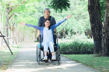 Asyalı bir çift, orta yaşlı bir koca karısına bakıyor, tekerlekli sandalyede oturan, parkta dinlenen, Asyalı bir aile ile ilişkisi olan bir hasta.