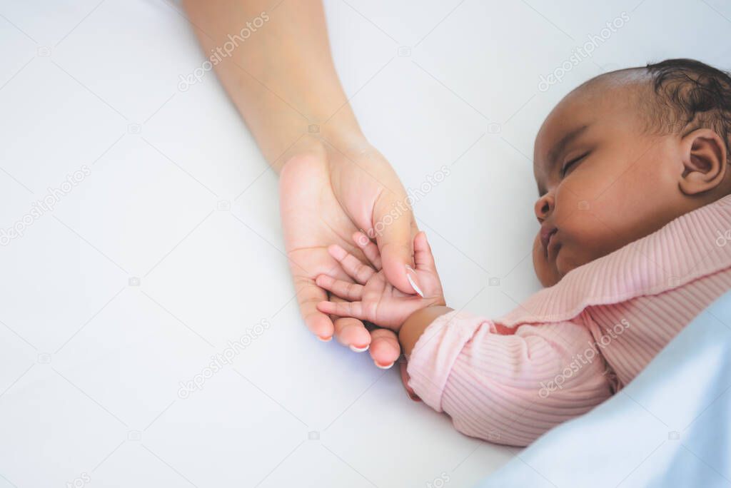 Blurred soft images, African American baby newborn is 3 months old, sleeping on white bed and mother holding her hand with love, to relationship in family and newborn concept.