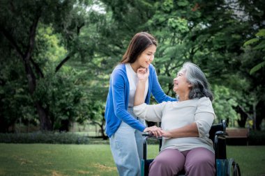 Asyalı bir aile, çekici bir kız. Annesine bakıyor ve bakıyor. Felçli bir hasta, tekerlekli sandalyede oturuyor, yeşil bahçede, aile ve sağlık sigortası konseptiyle ilişkisi var.