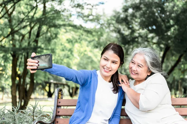 Asyalı bir aile, çekici bir kız ve yaşlı bir anne birlikte mutlu mesut vakit geçirir, yeşil bahçede dinlenir ve cep telefonuyla fotoğraf çeker, aile kavramı oluşturur ve doğayla baş başa tatil yapar..