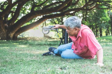 Tekerlekli sandalyeden düşüp yeşil çimlere uzanan yaşlı bir Asyalı, osteoartrit hastası..