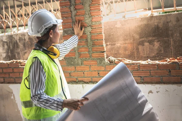 Asian woman construction engineer Checking the orderliness of the brick wall work, to meet the standards of the work, to workers and residential building construction concept.