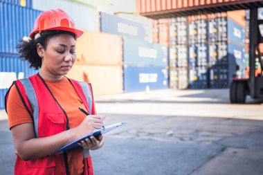 Afrikalı Amerikalı mühendis kadın bir rapor yazıyor ve konteynır endüstrisi, lojistik ulaşım ithalat-ihracat kargosunda çalışıyor, iş taşımacılığı ve depolama limanı terminali kavramına.