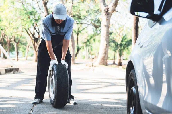 車のタイヤを変更するためにスペアタイヤを押すアジアの男性整備士は 道路上に駐車し 人々の旅行や交通の概念に — ストック写真